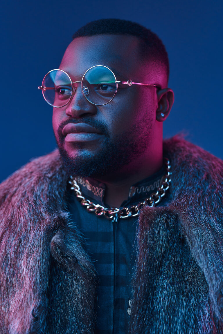 Portrait of rich african man dressed in fur coat and suit posing against dark background.