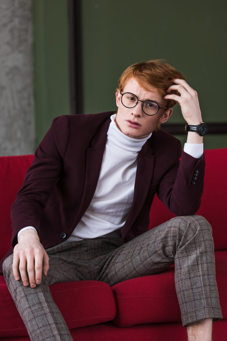 Portrait of young male fashion model in eyeglasses sitting on couch